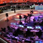 Journalists working at desks with multiple screens in a newsroom