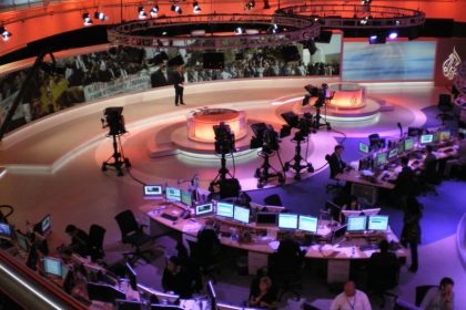 Journalists working at desks with multiple screens in a newsroom