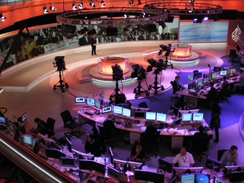 Journalists working at desks with multiple screens in a newsroom